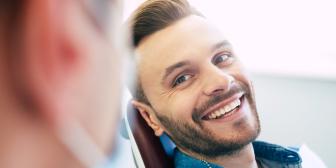 Junger Mann sitzt entspannt auf einem Behandlungsstuhl beim Zahnarzt und lächelt zufrieden in Richtung der behandelnden Person