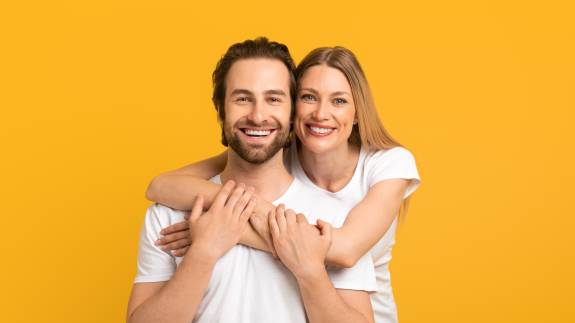 Glückliches Paar in weißen T-Shirts vor einem leuchtend gelben Hintergrund