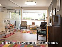 Modern eingerichtetes Wartezimmer mit bunten Teppichen, Retro-Möbeln, großen Fenstern und einem dekorativen Holzpferd.