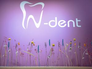 Logo der Zahnarztpraxis „N-dent“ an einer lila Wand mit stilisiertem Zahn-Symbol