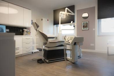 Moderner Behandlungsraum in einer Zahnarztpraxis mit einem ergonomischen Behandlungsstuhl, Deckenlampe und zahnmedizinischen Geräten.